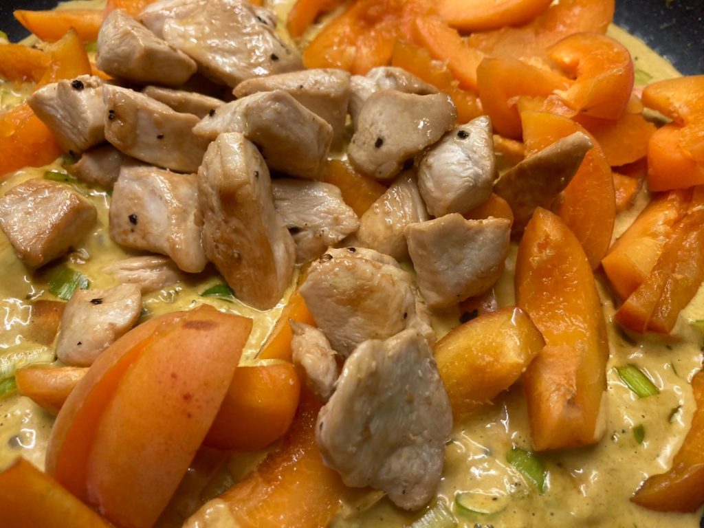 Hühnchen zum Gemüse und den Aprikosen in der Kokos-Curry-Sauce geben