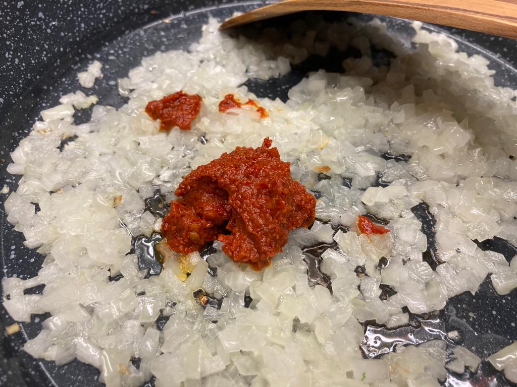 rote Currypaste zu den Zwiebeln in Kokosöl geben